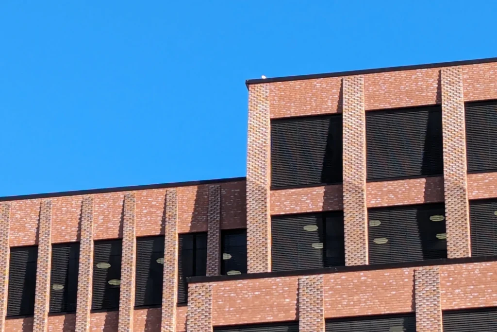 Building exterior with blue sky and sunlight, looking at the rooftop of the building, photograph of Domus Juridica in Oslo by Tobias Rade Evensen. 
